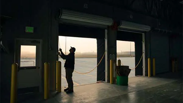 A worker opening a loading dock door at sunrise inside a warehouse.