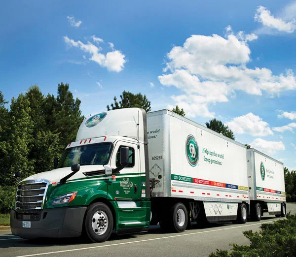 Old Dominion truck hauling expedited LTL freight on a sunny day with blue skies and trees.