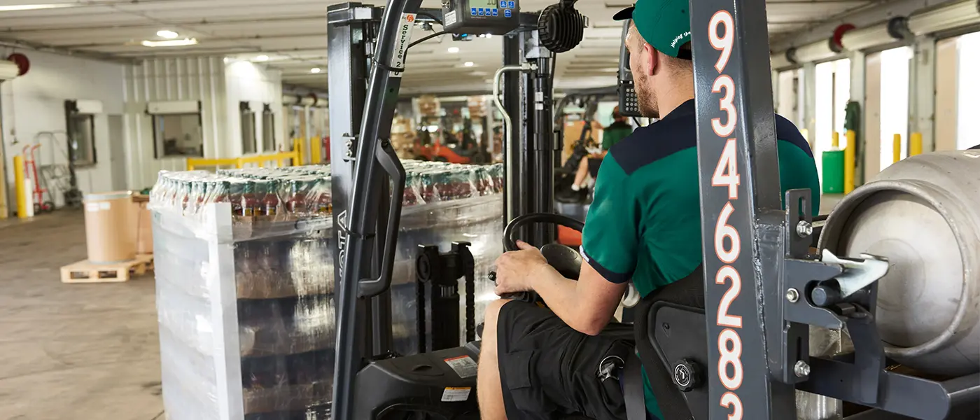 Forklift operator moving a pallet of bottled products in a warehouse for special rollout shipping.