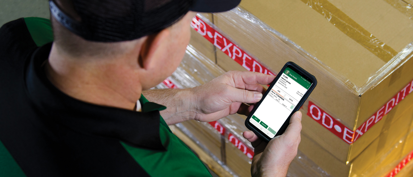 Driver using a mobile device to track MABD shipping for must-arrive-by-date freight delivery.