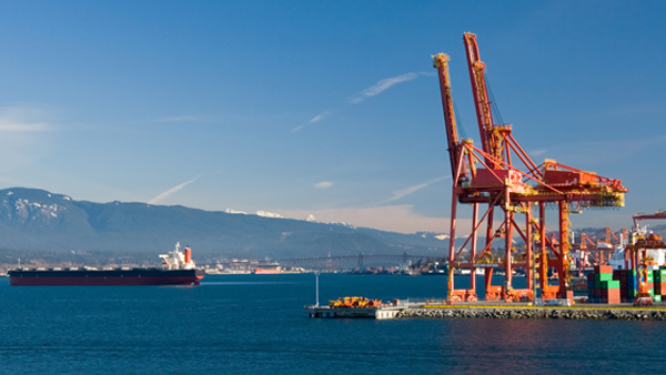 Cargo ship passing by cranes at an Alaskan shipping port, showcasing cargo shipping and drayage services.